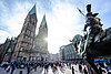 Der Bremer Dom im Sonnenschein, viele Menschen strömen über den Domshof. – 